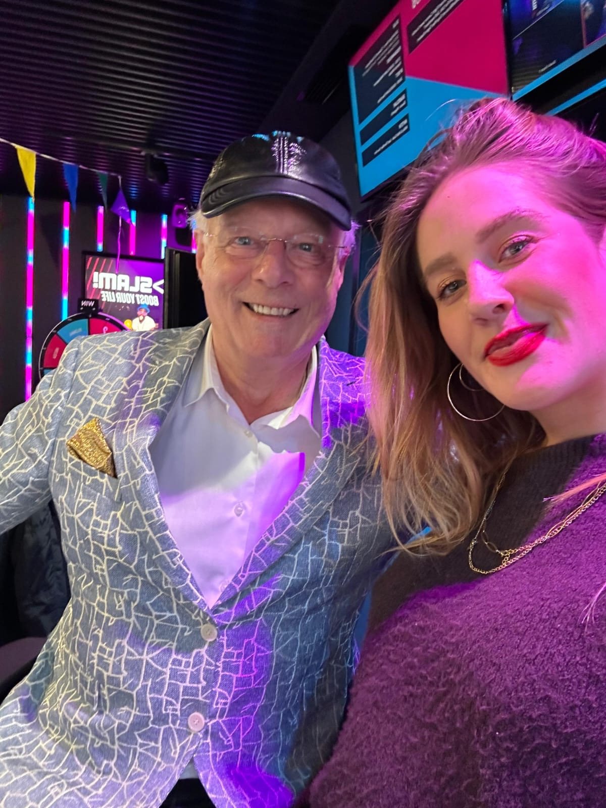 Selfie van Professor Drabb in blauw-wit gedessineerd colbert en zwarte pet met een jonge vrouw in de studio van SLAM!