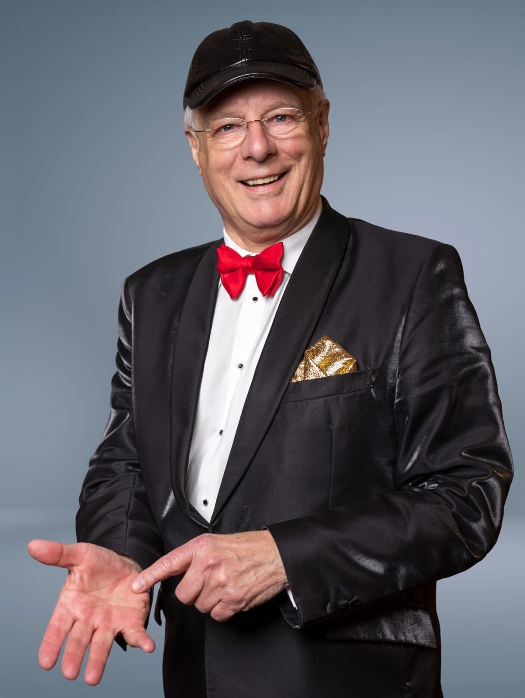 Studioportret van Professor Drabb in glanzende smoking met rode strik, gouden pochet en zwarte pet, wijzend naar zijn handpalm