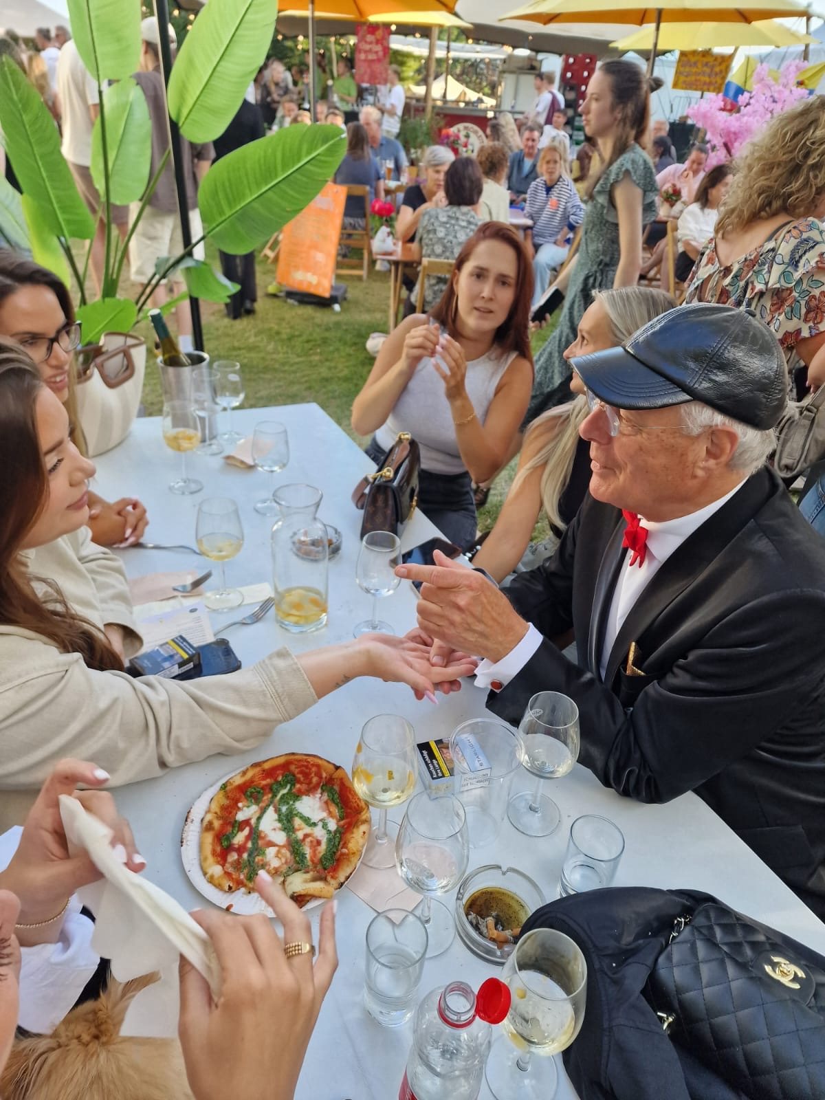Op een festivalterrein leest Professor Drabb aan een lange tafel de hand van een vrouw, terwijl anderen meekijken